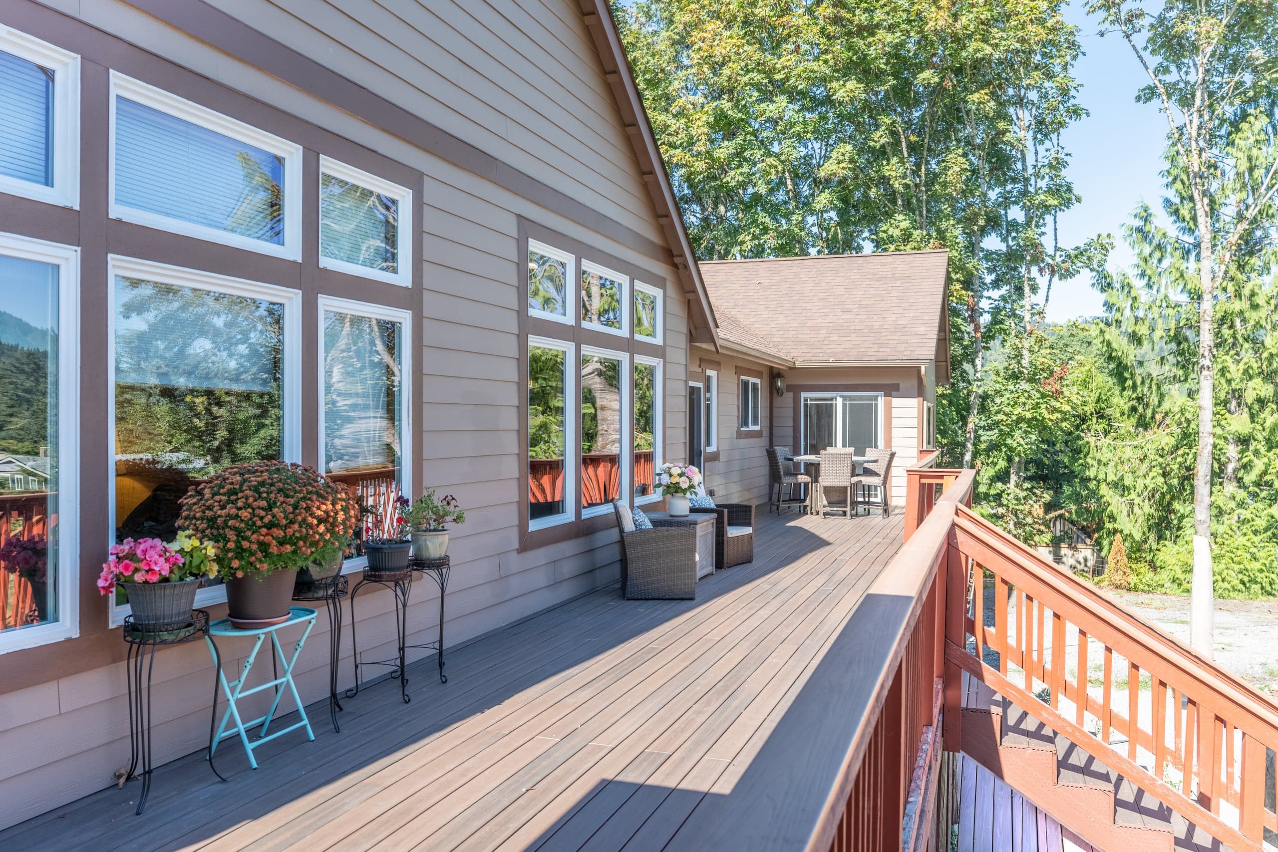 The long cedar deck running along the back of the house, with seating, potted chrysanthemums and a view over the valley.